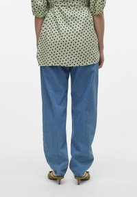 Blusa verde chiaro con motivo a cuori neri, abbinata a jeans in denim blu larghi e sandali con tacco verde oliva.
