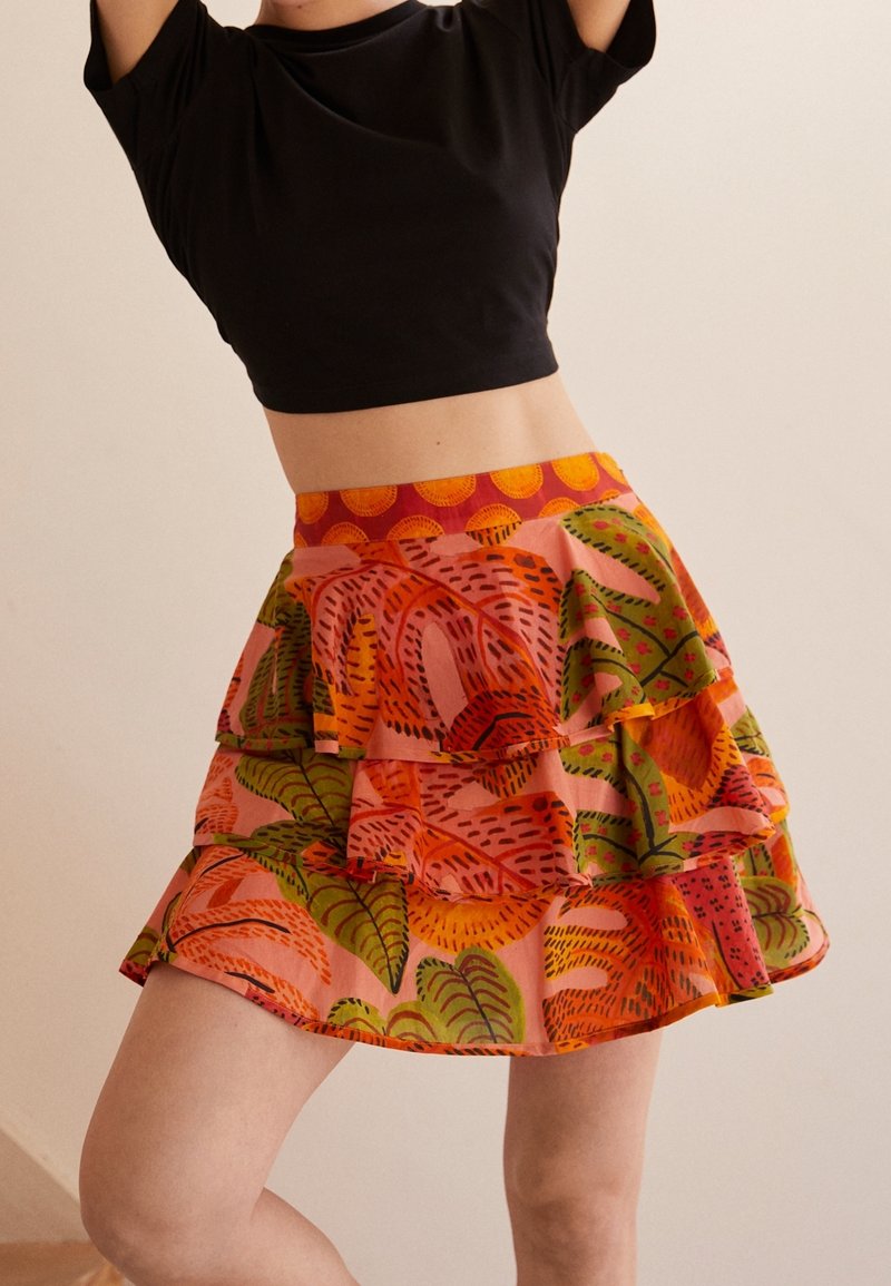 Barevná, vrstvená sukně vyrobená z lehkého materiálu, s růžovým pozadím a živými vzory zelených a oranžových listů.