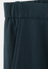 Granatowe spodnie z elastycznym pasem i kieszenią w szwie bocznym, ukazujące strukturę tkaniny i szczegóły szwów.