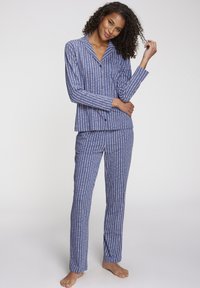 Pajama set u plavim i bijelim prugama koji se sastoji od košulje s kragnom i dugmadima te odgovarajućih hlača; tkanina se čini mekanom s laganom teksturom.