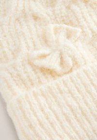 Tissu tricoté de couleur crème avec une texture douce et moelleuse présentant des côtes verticales et un petit détail en forme de nœud.