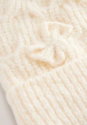 Krämfärgat stickat tyg med en mjuk, fluffig textur som har vertikala ribbade mönster och en liten rosett detalj.