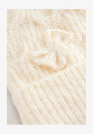 Krém színű kötött anyag puha, bolyhos textúrával, függőleges bordázattal és egy kis masni részlettel.