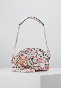 Sac à main floral de forme courbée, fabriqué en tissu texturé, présentant des motifs floraux roses et verts, des accents en chaîne argentée et une bandoulière amovible.