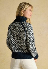Marineblaues und cremefarbenes gestricktes Sweatshirt mit floralem Muster, hohem geripptem Kragen und geripptem Saum, das strukturierte Details und kontrastierende Farben zeigt.