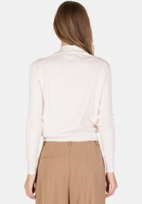 Maglione aderente color beige chiaro con maniche lunghe e orlo a coste, realizzato in materiale morbido. Abbinato a pantaloni beige a vita alta.