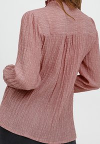 Rosa strukturierte Bluse mit langen Ärmeln, gerafft an den Schultern, mit einem leicht lockeren Schnitt und einem dezenten, zerknitterten Muster.
