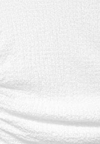 Texturovaná bílá tkanina s vrásčitou plochou, která vykazuje jemnou hloubku a rozměr díky mírným záhybům a vlnkám.