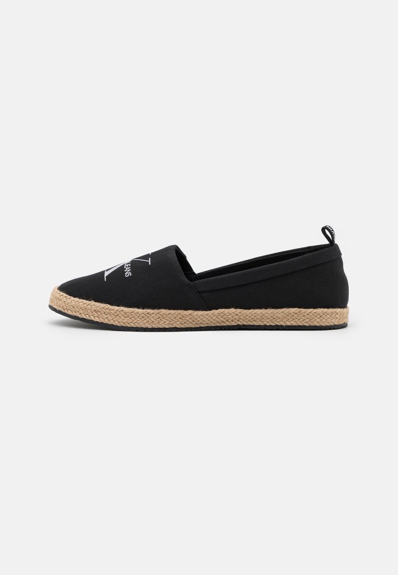 Espadrille noire sans lacets avec semelle tressée beige et logo de la marque blanc sur le dessus, vue de côté sur un fond uni.