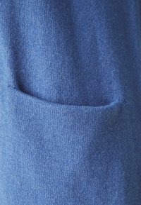 Primer plano de un suéter azul con un tejido texturizado, que presenta un gran bolsillo frontal y un acabado suave. La tela parece cálida y acogedora.