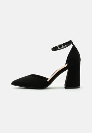 Black suede high-heeled pump with a pointed toe, ankle strap with a buckle, and a chunky heel. Smooth texture; simple design.