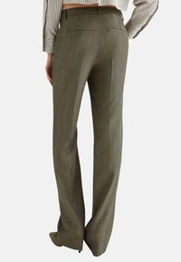 Pantaloni verde oliva con una tessitura strutturata, caratterizzati da un taglio dritto e due tasche posteriori, con vita alta e sottili pieghe.