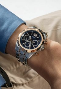 Orologio cronografo con quadrante blu, dettagli in oro rosa, cinturino in acciaio inossidabile e sottodial dettagliati; presenta numeri grandi e una lunetta testurizzata.