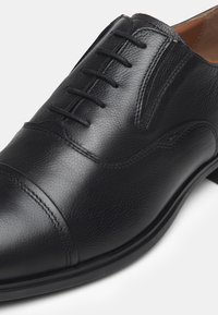 Chaussure habillée en cuir noir avec un bout arrondi, un laçage, des détails de couture subtils et une finition lisse et texturée.