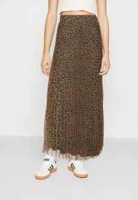 Falda maxi de estampado de leopardo con diseño plisado y cintura elástica, hecha de un material ligero; combinada con zapatillas blancas con acentos en negro.