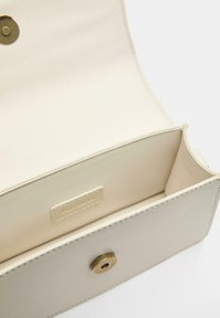 Notranjost kreme barvne torbice z gladko tkaninsko podlogo, zapiranjem na zlato kovinsko sponko in prikritim logotipom na priponki.