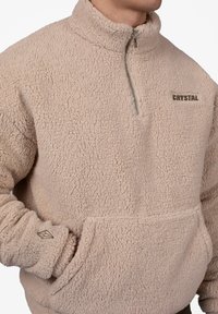 Beiger Fleece-Pullover mit Viertel-Reißverschluss, strukturiertem Material, Brusttasche und besticktem "CRYSTAL"-Logo in Braun. Akzentuierte Bündchen.