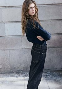 Jeans in denim scuro con cuciture gialle, vita alta, gamba dritta e design a cinque tasche, abbinati a una camicia aderente in denim scuro.