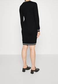Abito nero in maglia con maniche lunghe, silhouette aderente e strisce bianche a contrasto sul colletto e sui polsini. Indossato con mules neri a tacco blazer.