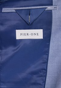 Marinefarbener Stoff mit einem subtilen Glanz, texturiertem Finish und einem blauen Etikett mit der Aufschrift "PIER•ONE." Verfügt über eine kleine Tasche oberhalb des Etiketts.