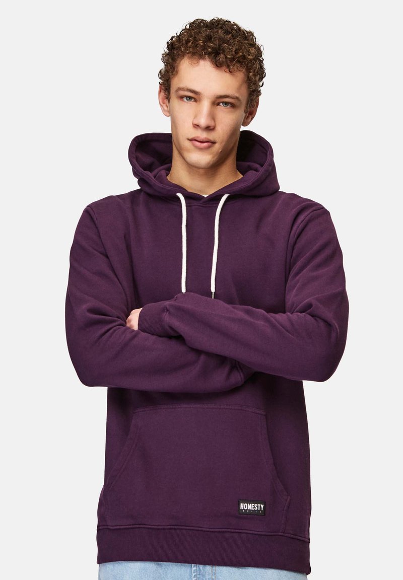 Lila hoodie i mjukt tyg, med en framlapp, justerbar dragsko på huvan och kontrasterande vita snören. Märkesetikett vid fållen.