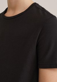 Svart bomulls-T-shirt med rund halsringning och korta ärmar. Mjuk textur med sydda ärmslut. Minimalistisk design.