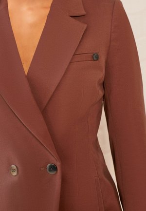 Blazer marrone doppiopetto realizzato in tessuto testurizzato, con colletto a scollo a V, bottoni neri e una tasca sul petto.