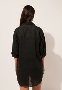 Vestito chemisier in lino nero con colletto, maniche arrotolate e dettaglio di spacco sul retro, caratterizzato da una vestibilità ampia e tessuto testurizzato.