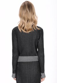 Maglione grigio a coste con design aderente, caratterizzato da corpo più scuro e dettagli lavorati a maglia più chiari di grigio sull'orlo e sui polsini. Dettaglio della superficie testurizzata.