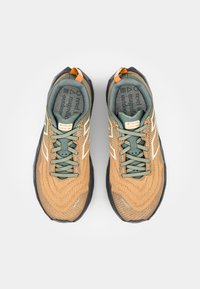 Scarpe da atletica marroni e verdi con una tomaia in mesh testurizzato, suola nera, accenti bianchi e un laccio sul tallone arancione a contrasto.