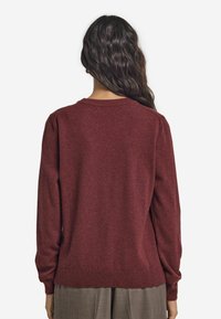Bordeauxroter Pullover mit langen Ärmeln, gerippten Bündchen und Saum, aus einem weichen, strukturierten Stoff gefertigt. Klassischer Rundhalsausschnitt und nahtloser Rücken.