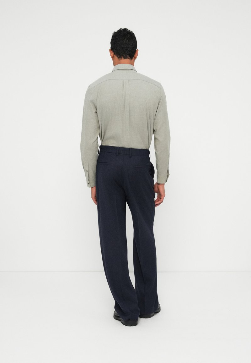 Light gray button-up shirt with a structured collar, paired with dark navy trousers. The fabric appears textured with a tailored fit.