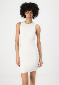 Ribaga, ilma varrukat valge kleit, millel on ümmargune kaelus ja külje lõhikud. Omab musta ääristust õmbluste ääres visuaalse kontrasti jaoks.