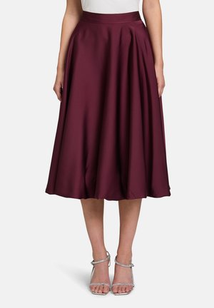 Jupe bourgogne, longueur genoux, en tissu lisse avec des plis, dotée d'une large taille. Associée à des talons argentés à lanières.