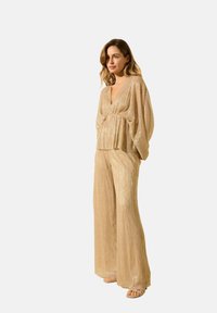 Ensemble en tissu léger doré, comprenant un haut à décolleté en V profond avec des manches larges et un pantalon fluide à jambes larges assorti. Texture lisse et scintillante.