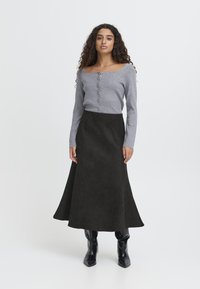 Maglione grigio aderente con scollatura quadrata e chiusura a bottoni, abbinato a una gonna nera in suede a trapezio e stivali neri lucidi alti fino al ginocchio.