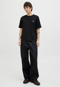 Sort t-shirt med korte ærmer og et pink grafik på brystet, parret med løstsiddende mørkeblå jeans og mørkebrune sko.