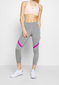Grå atletiske leggins med pink accentstriber, parret med en lyserød sports-bh. Begge items har Nike-branding og en tætsiddende design.