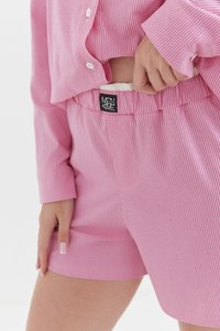Różowe spodenki piżamowe w paski, wykonane z miękkiego materiału, z elastycznym pasem i metką z logo z tyłu. Dołączona koszulka ma dopasowane paski.