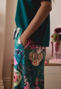 Zielone spodnie piżamy mają żywy kwiatowy wzór z różowymi akcentami. Miękka tkanina i elastyczny pasek w talii zapewniają luźny krój i komfort.