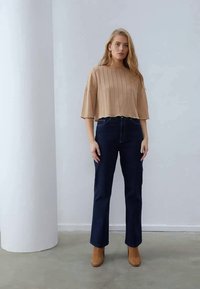 Beige, bordázott, rövid ujjú felső, laza szabással, sötétkék, magas derekú farmernadrággal párosítva. Barna velúr bokacsizma teszi teljessé a szettet.