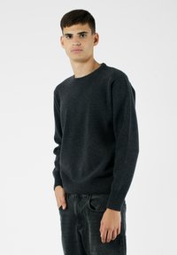 Ciemnoszary sweter z długim rękawem, okrągłym dekoltem, ściągaczami na rękawach i u dołu; wykonany z teksturowanej tkaniny, zestawiony z ciemnymi dżinsami.