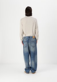Beige langærmet skjorte og løse blå denim jeans med et falmet mønster. To baglommer og et lædermærke på taljebåndet.