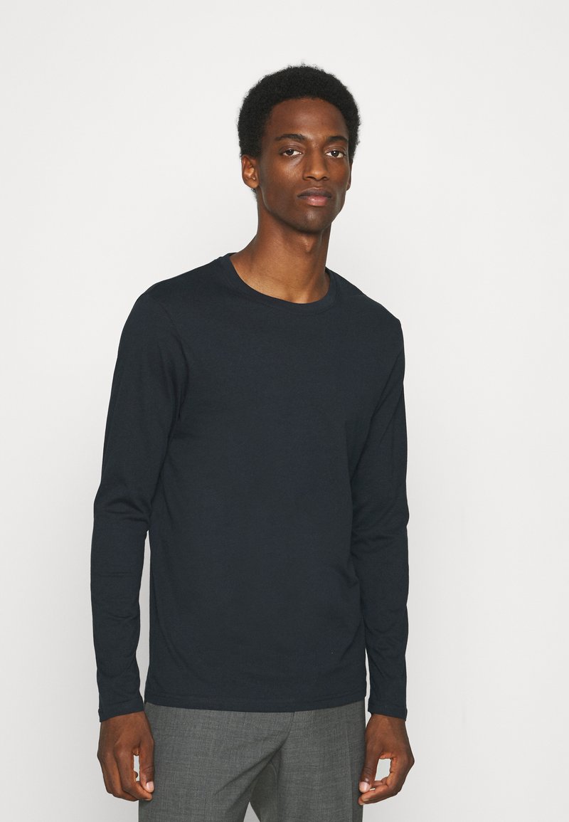 Langärmliges, dunkelblaues Hemd aus weichem Stoff mit Rundhalsausschnitt. Verfügt über ein schlichtes Design und eine lockere Passform. Kombiniert mit grauen Hosen.