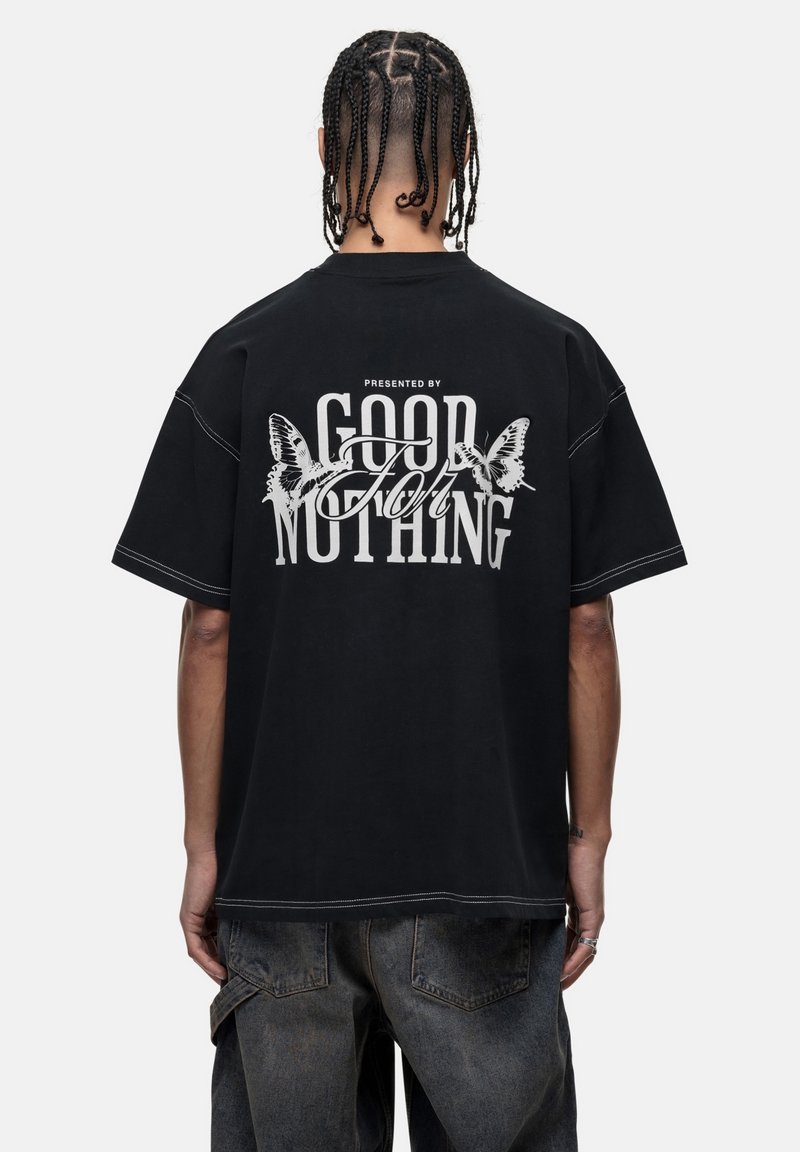 T-shirt noire surdimensionnée avec un texte graphique blanc au dos, agrémenté de motifs de papillons et de détails de couture contrastants.