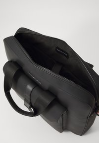 Czarna torba na laptopa wykonana z trwałego materiału, z zamkiem błyskawicznym, uchwytem na górze oraz wewnętrzną metką. Gładka tekstura o eleganckim designie.
