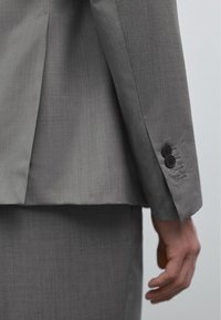 Grauer, maßgeschneiderter Anzugjacke mit glatter Stoffstruktur, zwei schwarzen Knöpfen am Ärmel und dezenten Nähdetails.