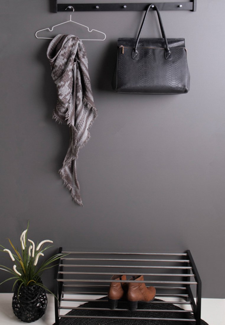 Porte-manteau en métal noir avec des crochets, écharpe grise à motif, sac à main noir texturé, bottines marron à la cheville sur un range-chaussures à lattes, et une plante.