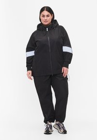 Black waterproof jacket with a hood, featuring white stripe accents. Paired with black pants and athletic shoes, designed for active wear.