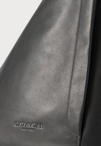 Graue Lederhandtasche mit glatter Textur. Verfügt über ein sichtbares Logo und dezente Steppnähte entlang der Kanten.